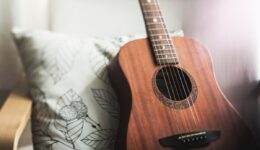 acoustic guitar sitting upright against a pillow on a couch