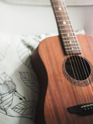 acoustic guitar sitting upright against a pillow on a couch